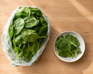 A close-up, angled photograph of a person's hands (cropped, no face) portioning bulk-purchased meat into individual freezer bags on a kitchen counter. Natural daylight, warm neutral tones, no text, no logos, realistic editorial lifestyle photography style.